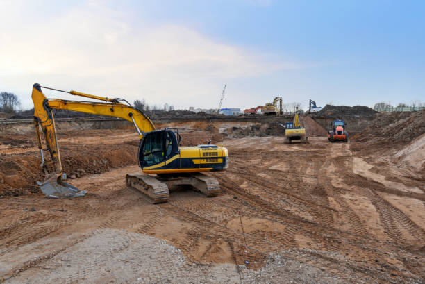 Excavator on earthworks at construction site. Backhoe on road construction. Tower cranes in action on blue sky background. Heavy machinery and construction equipment